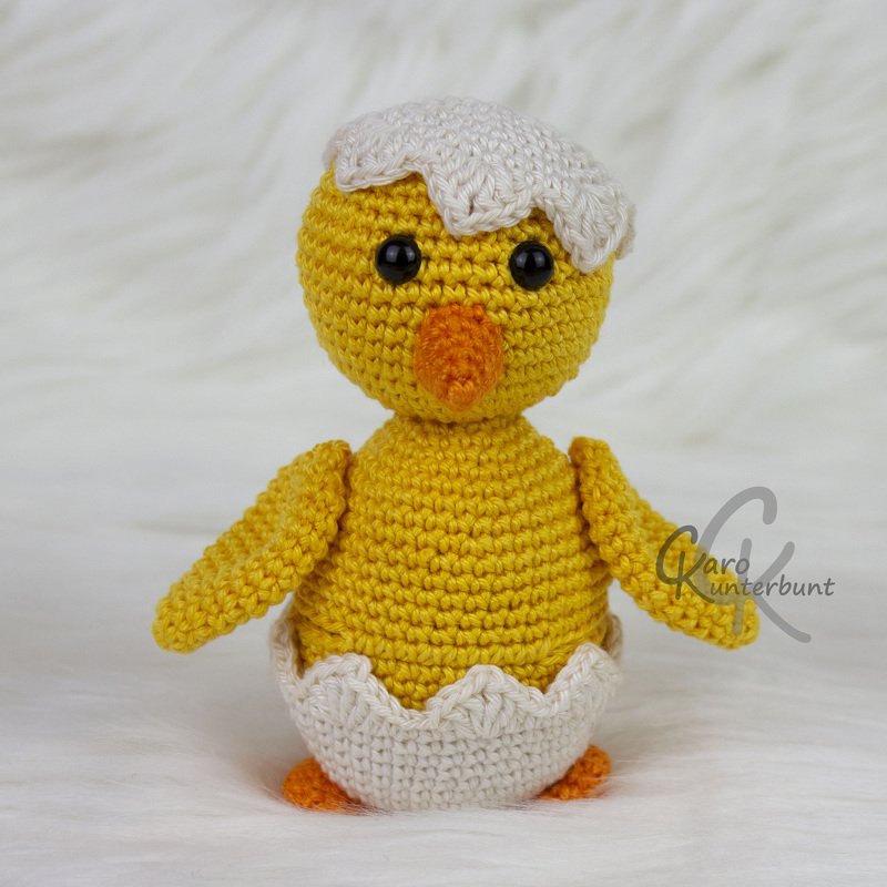 Gehäkeltes gelbes Küken mit weißer Eierschale auf hellem Hintergrund