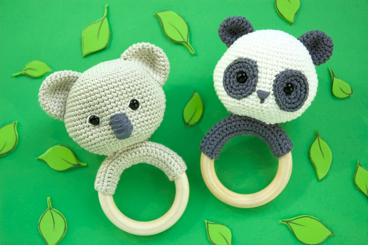 Gehäkelter Koala- und Panda-Greifring mit Holzring auf grünem Hintergrund