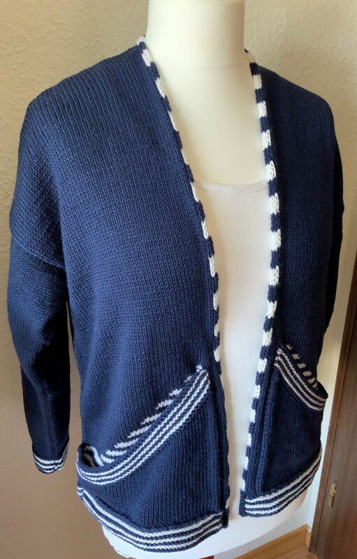 Dunkelblaue gestrickte Damen-Strickjacke mit weißen Streifen an Saum, Taschen und
Ärmeln auf einer Schaufensterpuppe.