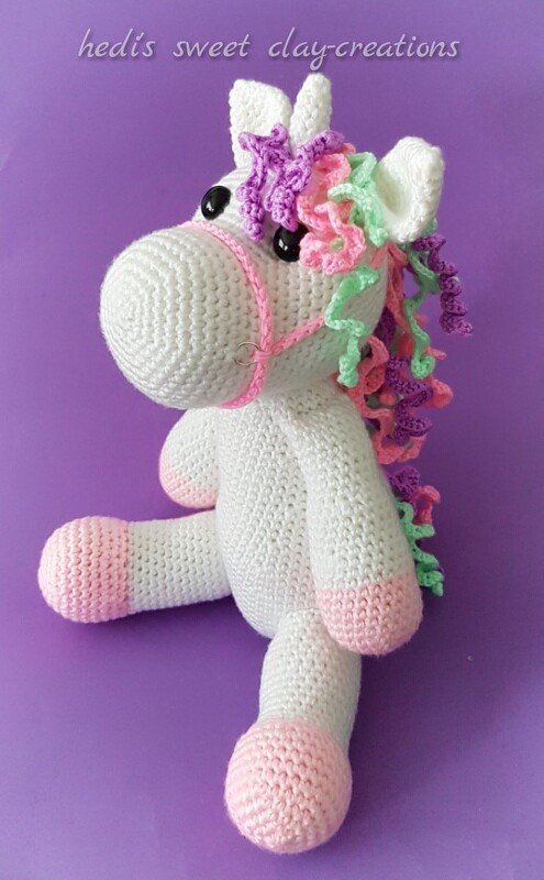 Weißes handgehäkeltes Amigurumi-Einhorn mit lockiger Pastellmähne (Lila, Rosa, Mint) und rosa Hufen