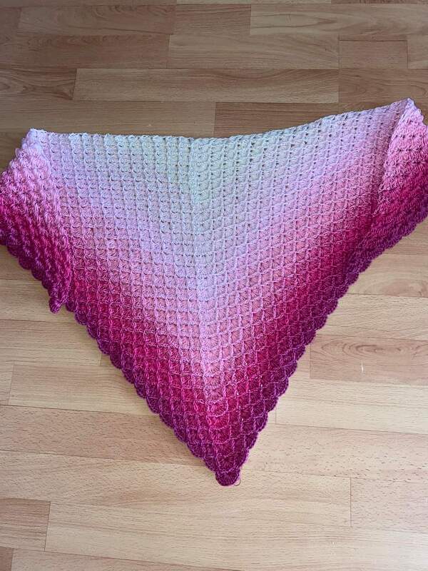 Gehäkeltes Dreieckstuch mit Creme- bis Magenta-Farbverlauf und Muschelmuster, auf Holzboden ausgebreitet