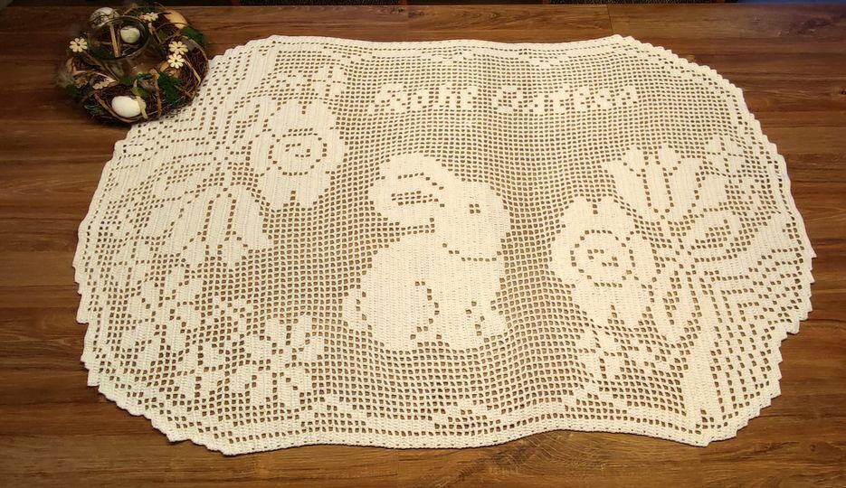 Ovaler cremefarbener Tischläufer gehäkelt mit Osterhase, Blumen und 'Happy Easter' Schriftzug auf Holztisch.