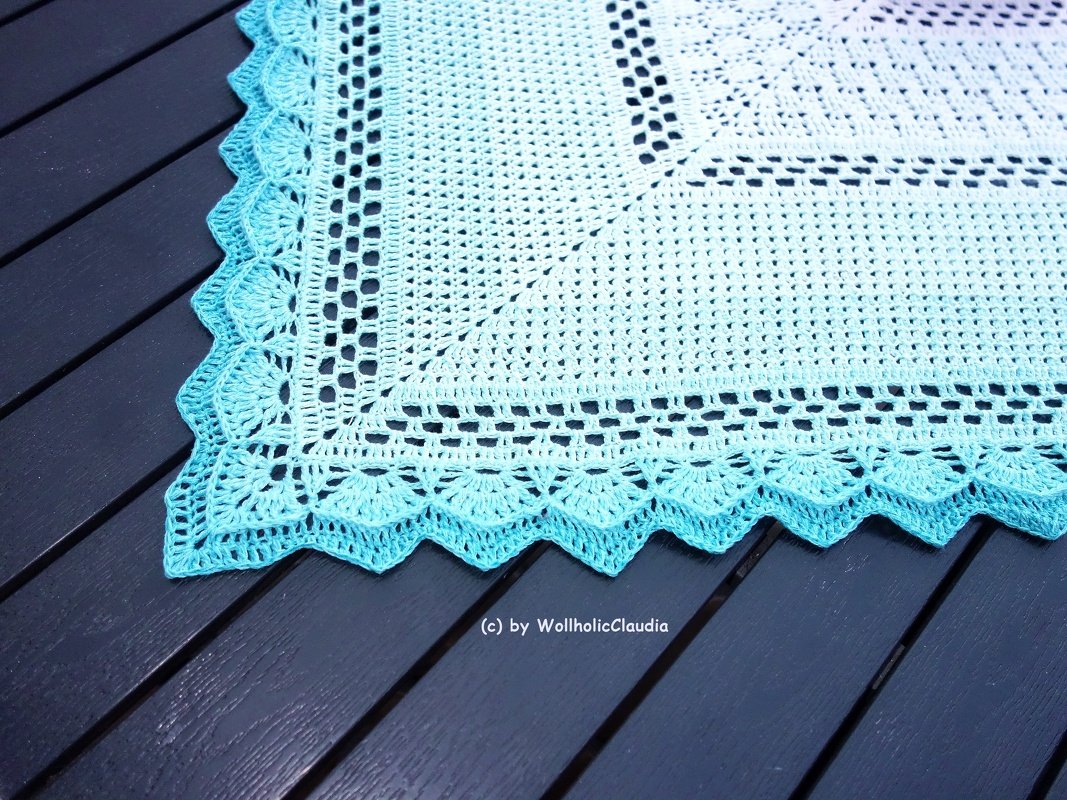 Eckdetail eines gehäkelten Tischläufers mit Weiß‑Türkis‑Verlauf und Muschelkante auf dunklem Holztisch
