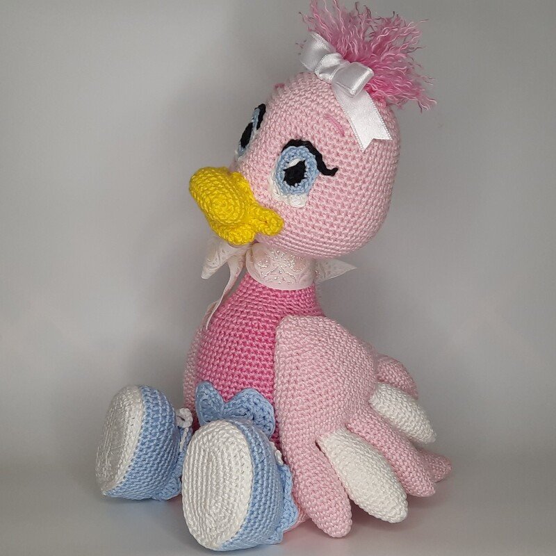 Rosa gehäkeltes Amigurumi-Entchen mit gelbem Schnabel, weißer Schleife, gestickten Augen und blau-weißen Häkelschuhen