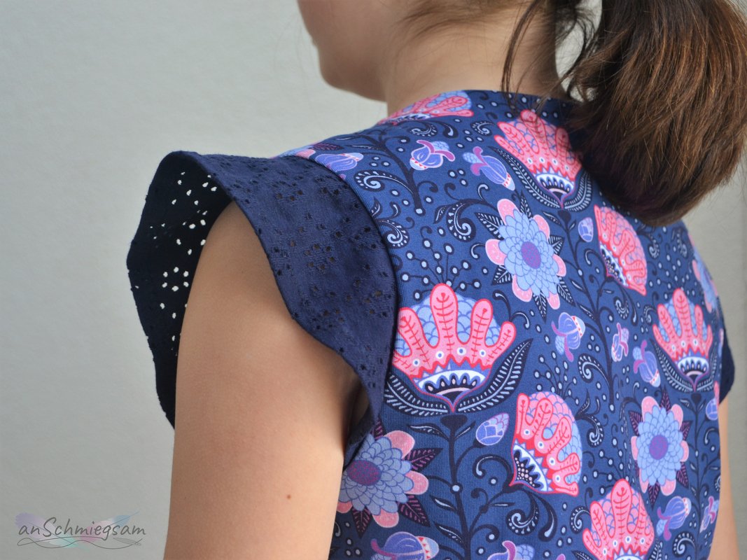 Rückenteil eines Kinderkleids mit floraler Stoffbahn und dunkelblauen Lochstickerei-Ärmeln
