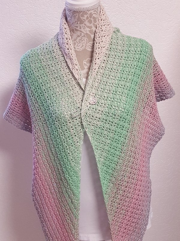 Gehäkeltes Dreieckstuch in Pastellfarben auf Schaufensterpuppe als Poncho mit Knopf