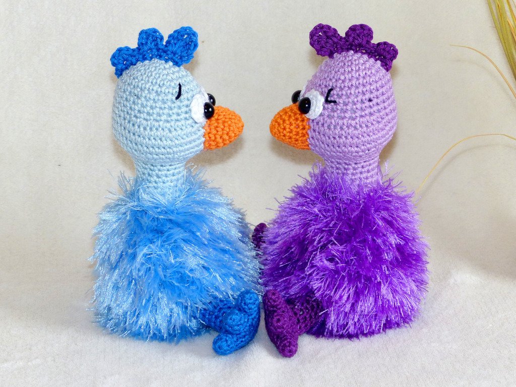 Seitenansicht zweier Amigurumi‑Vögel mit fransigem Garnkörper und orangefarbenen Schnäbeln