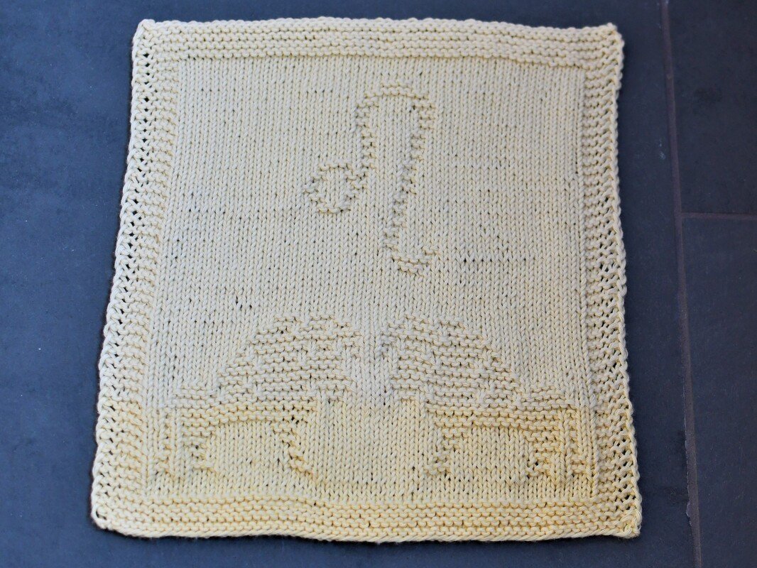 Beiges gestricktes Quadrat mit reliefartigem Motiv: Auto, Ballon und Musiknote