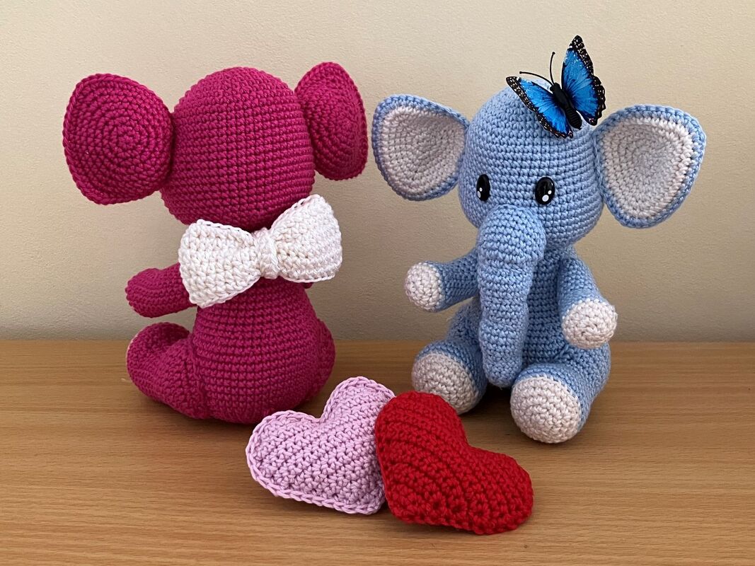 Detailansicht zweier gehäkelter Amigurumi‑Elefanten mit Ohren, Rüssel, Schleife und zwei Herz-Amigurumis