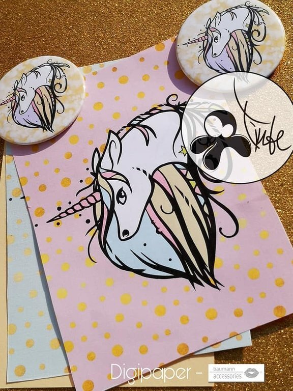 Stylized white unicorn with pastel mane and horn on pink paper with gold polka dots, next to two round unicorn buttons