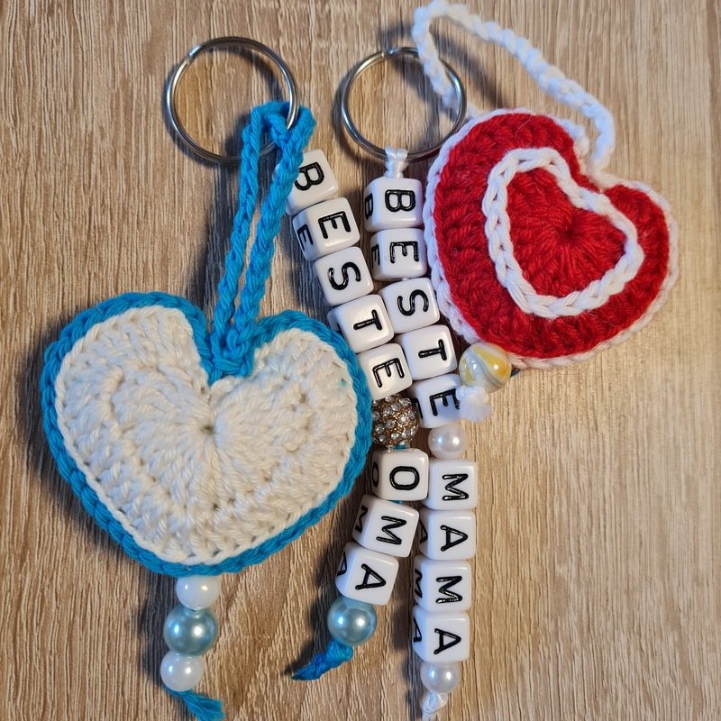 Zwei gehäkelte Herz‑Schlüsselanhänger (weiß‑blau, rot‑weiß) mit Perlen und Buchstabenwürfeln ‚BESTE OMA‘ und ‚MAMA‘
