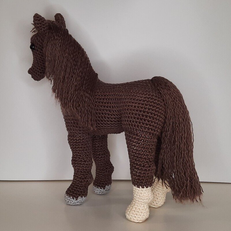 Gehäkeltes braunes Amigurumi-Pferd mit langer Mähne und hellen Unterschenkeln, seitliche Ansicht