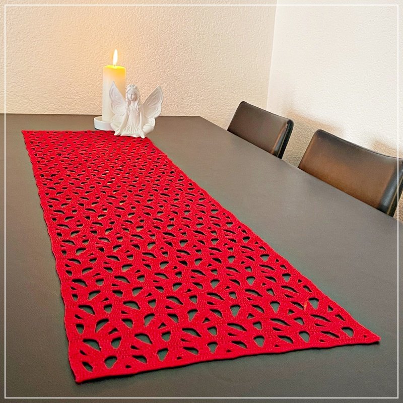 Rectangular red crochet table runner with repeating leaf openwork on a dark dining table, candle and angel ornament at one end