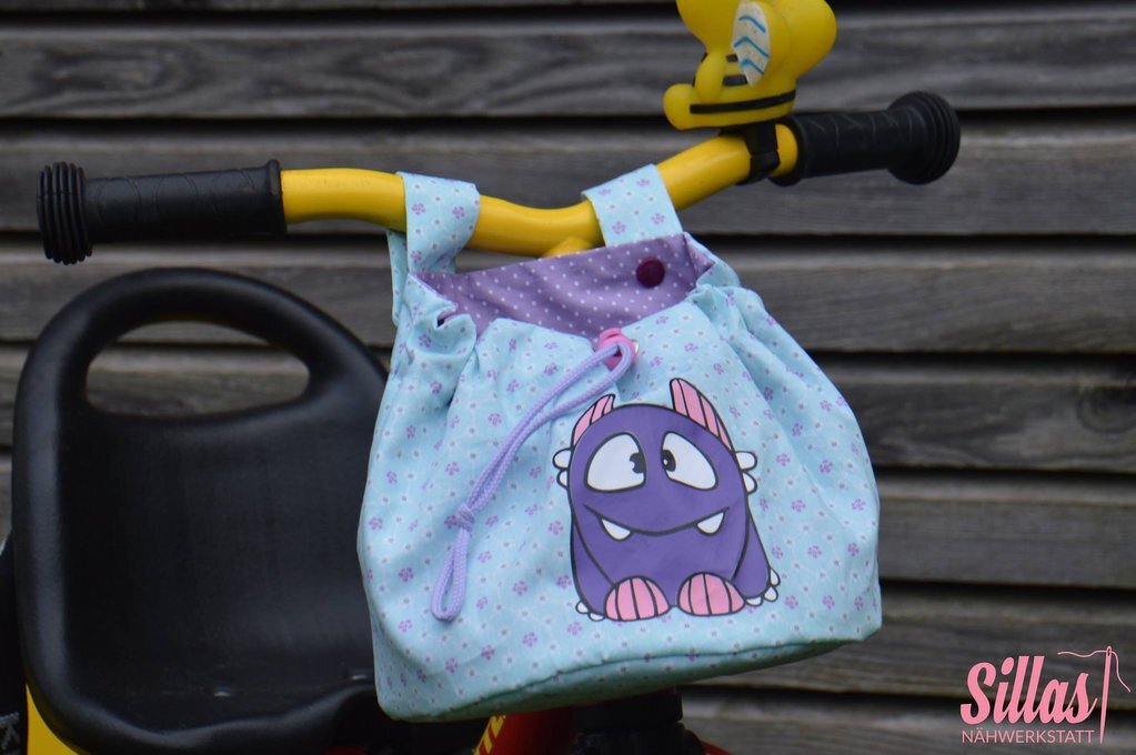 Light-blue drawstring handlebar bag with purple cartoon monster attached to yellow bike handlebars