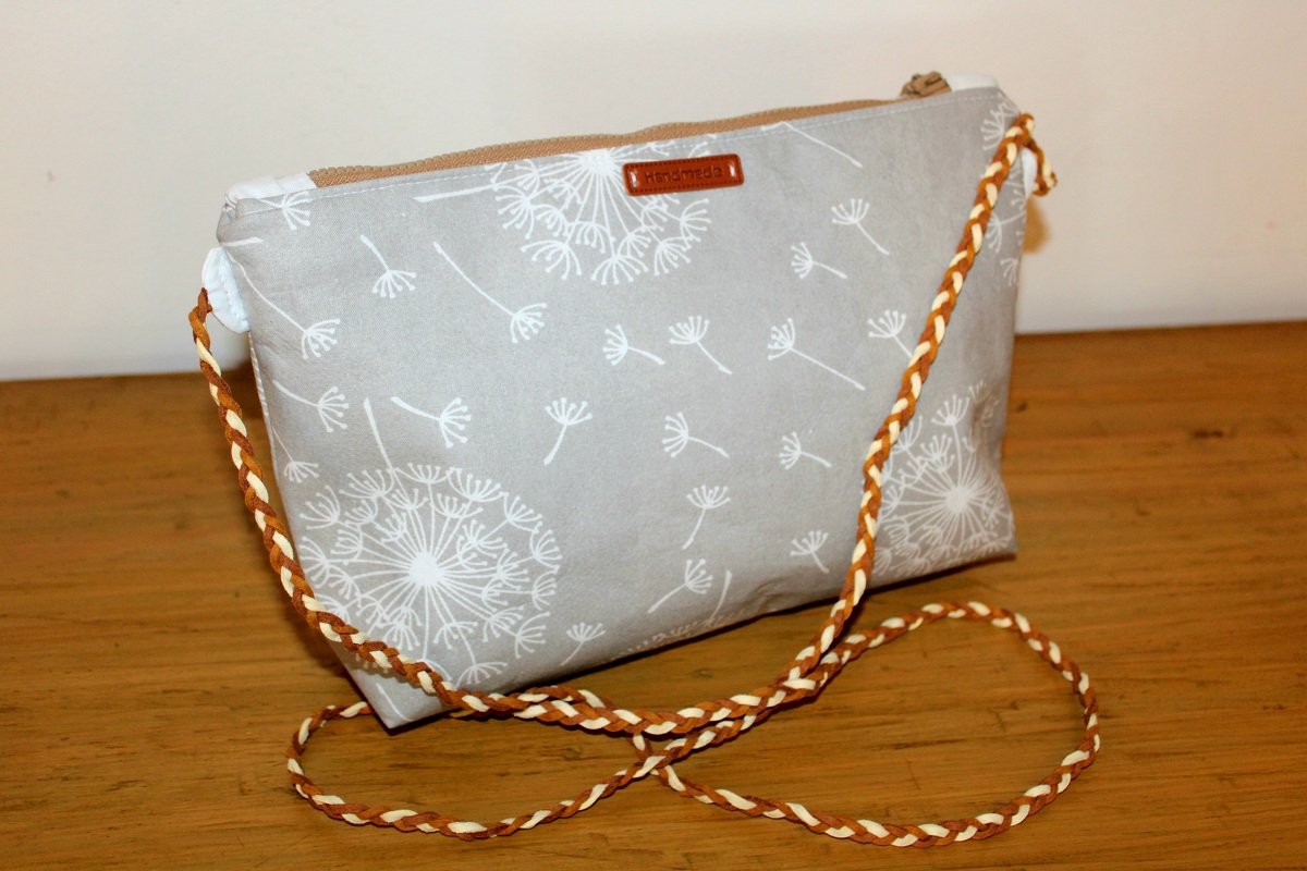 Grau-beige genähte Tasche mit Reißverschluss, weißem Pusteblumenprint und geflochtenem braun-beigem Trageriemen