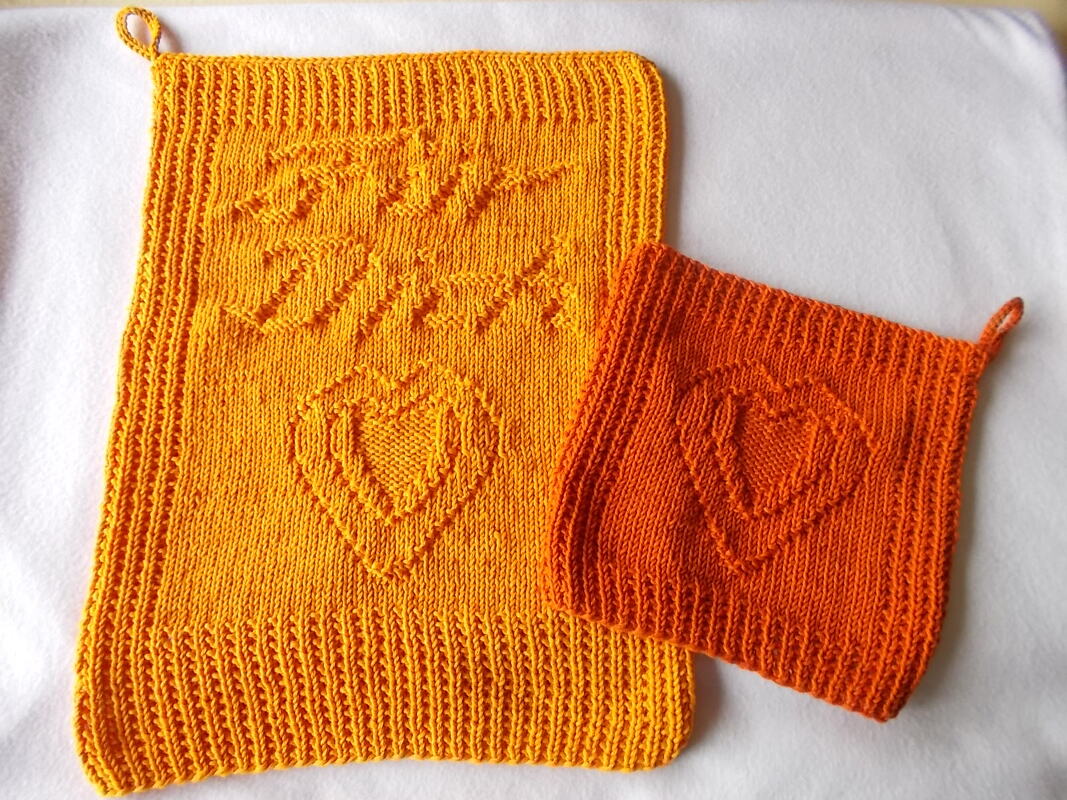 Zwei gestrickte Topflappen in Gelb und Orange mit Herzmotiv, geripptem Rand und Aufhängeschlaufen