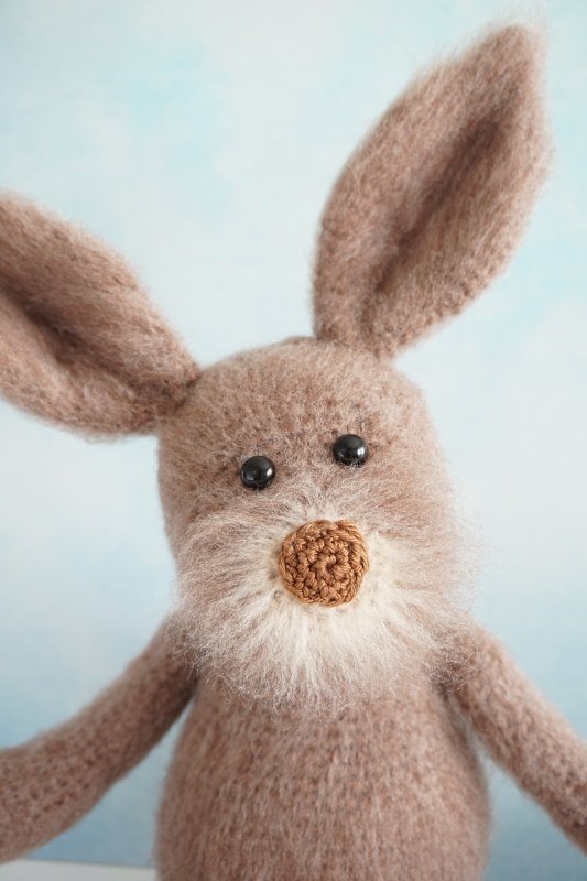 Nahaufnahme eines gehäkelten braunen Amigurumi-Hasen mit langen Ohren, schwarzen Augen und flauschiger Schnauze vor hellem Hintergrund.