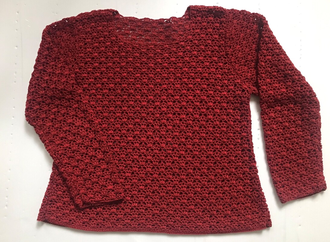 Roter gehäkelter Damenpullover mit Muschelmuster, flach auf hellem Untergrund