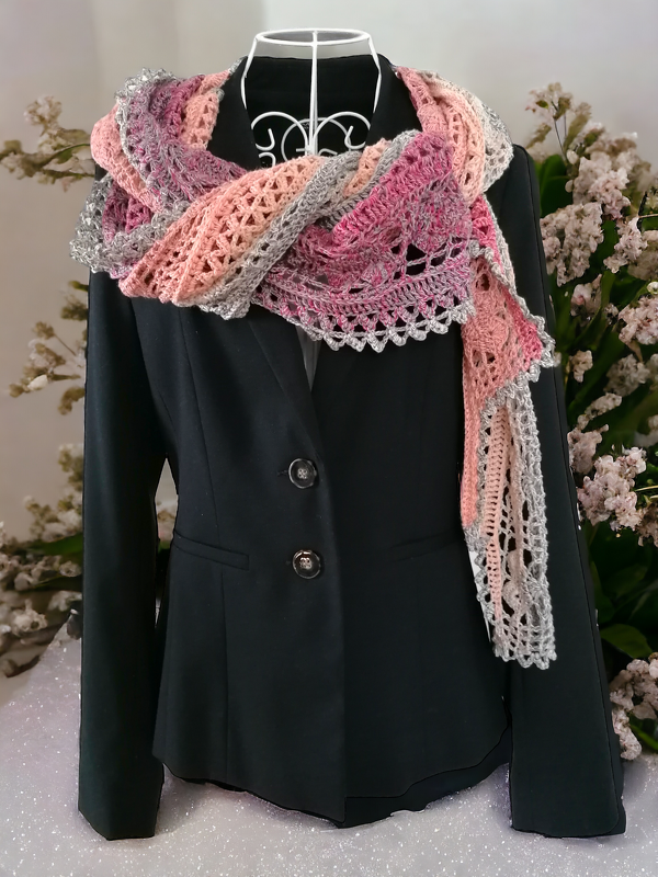 Crocheted shawl in pink, peach, and grey with openwork lace pattern and scalloped edge, displayed on a mannequin wearing a black blazer.