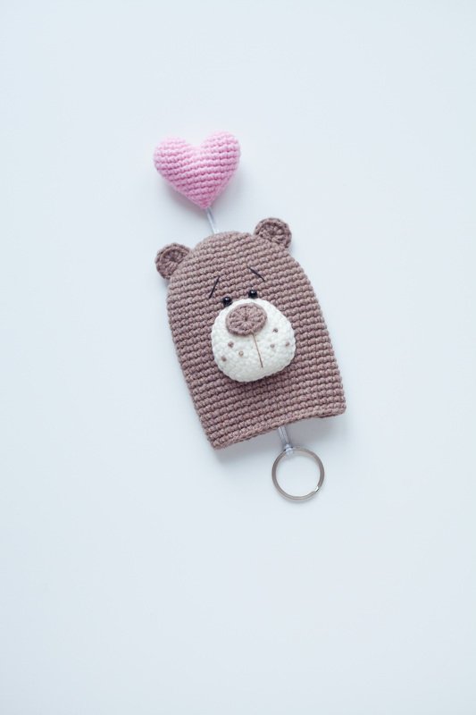 Brown crocheted bear keychain with white muzzle, embroidered eyes, and a pink heart balloon attached to a metal key ring