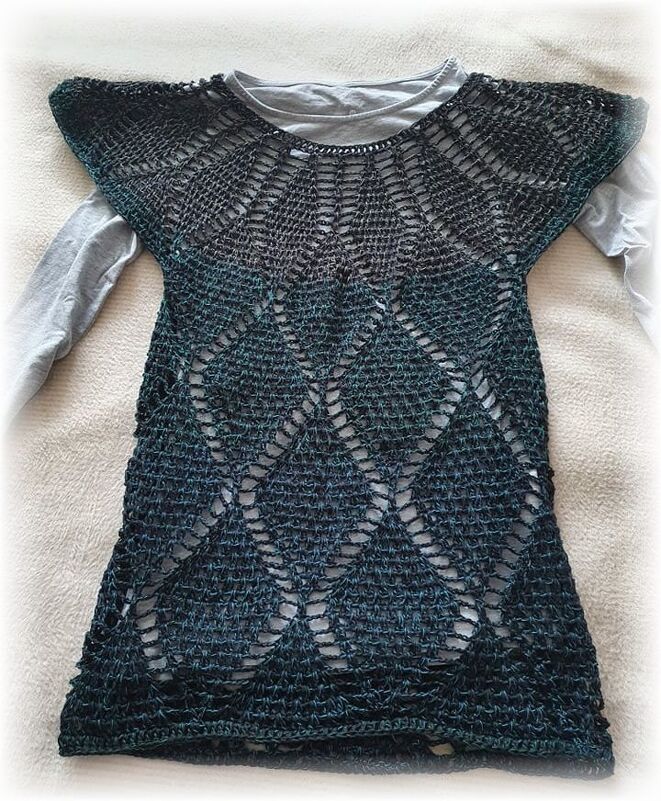 Dunkelgrüne, gehäkelte Damen-Tunika mit offenem Rautenmuster über einem grauen Langarmshirt.