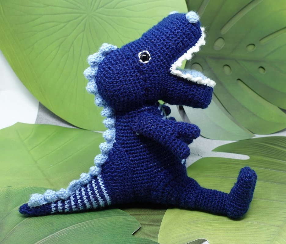 Sitzender gehäkelter blauer Dinosaurier mit hellblauen Zacken