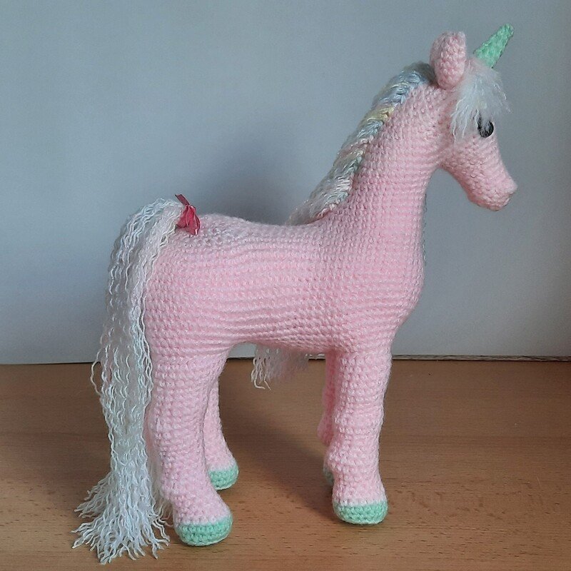 Stehendes rosa Amigurumi‑Einhorn mit langer weißer Mähne und mintfarbenen Hufen