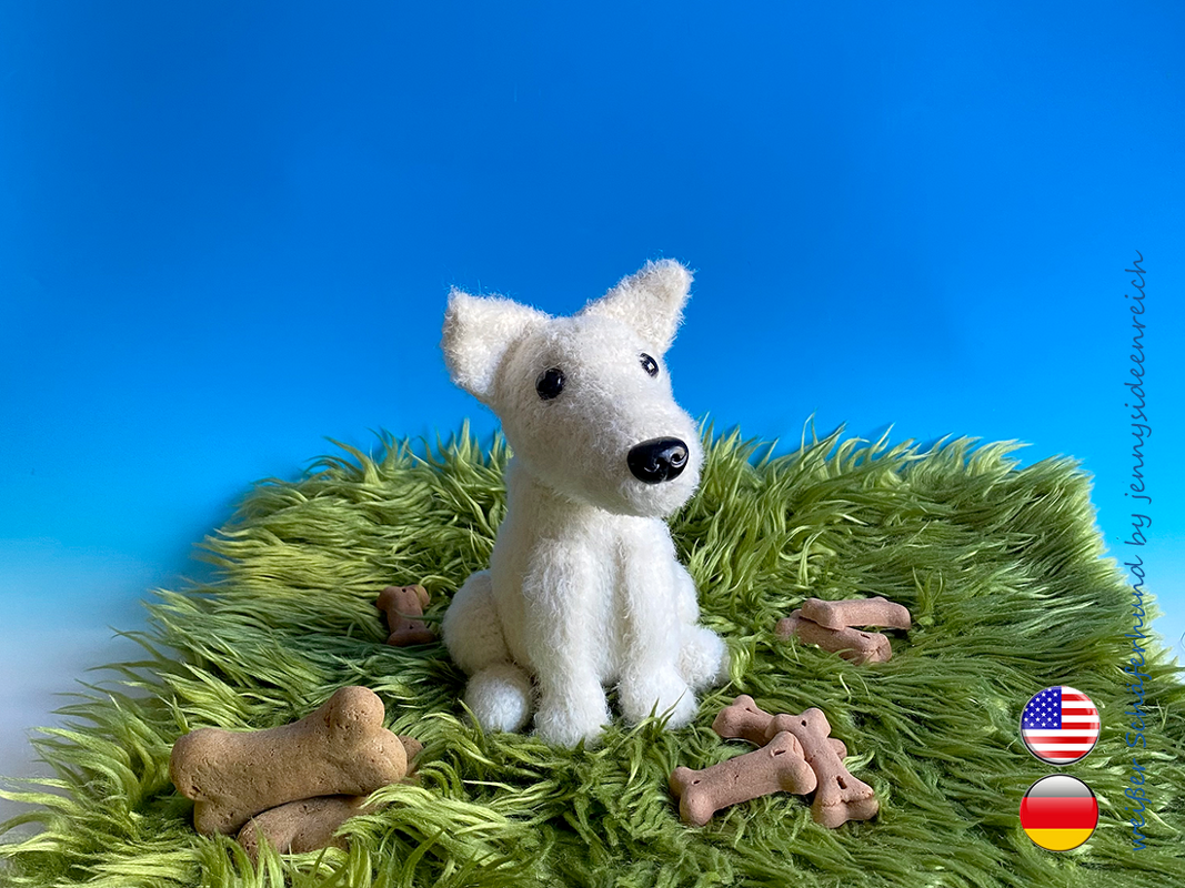 sitzender weißer Amigurumi-Hund mit spitzen Ohren und schwarzer Nase auf grünem Teppich