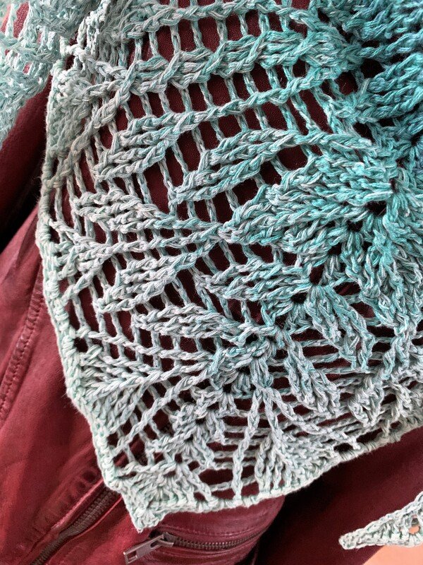 Close-up of a teal crochet triangle shawl with lacy openwork draped over dark red fabric.