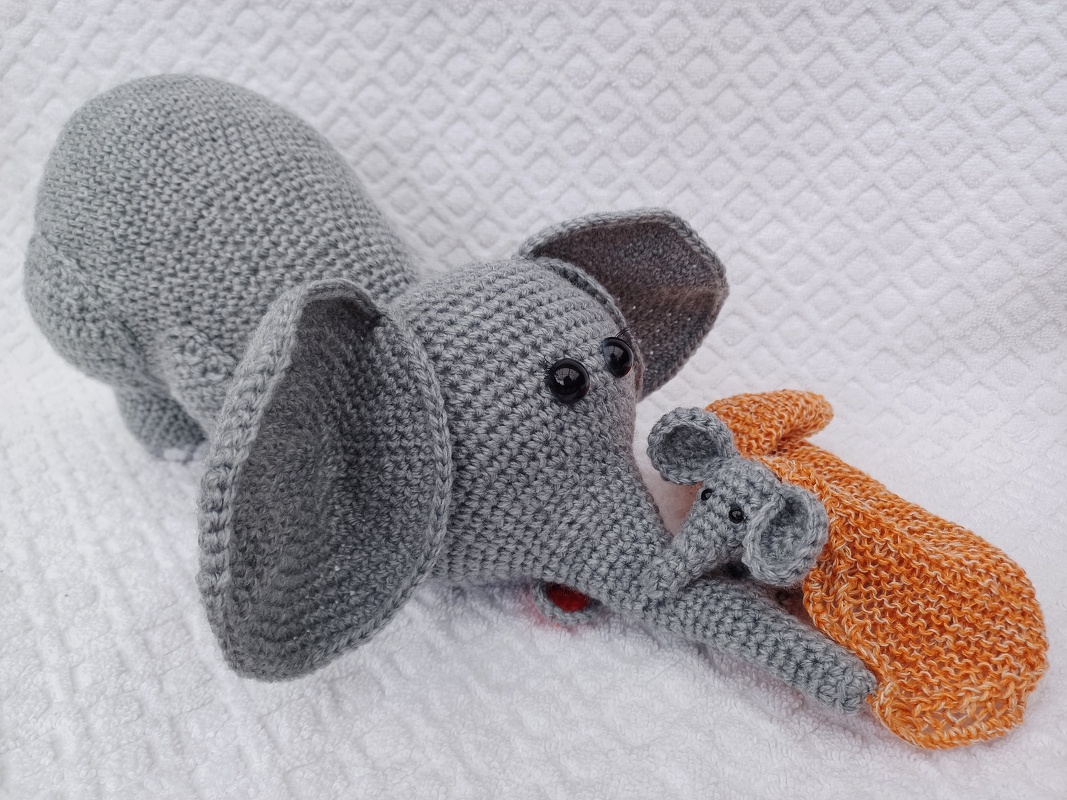 Gehäkelter grauer Elefant mit großen Ohren und kleinem Elefantenbaby, neben orangefarbenem Häkelstück