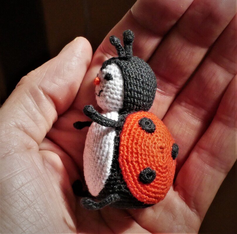 Palm-sized crochet ladybug amigurumi with red shell, black spots and antennae held in a hand