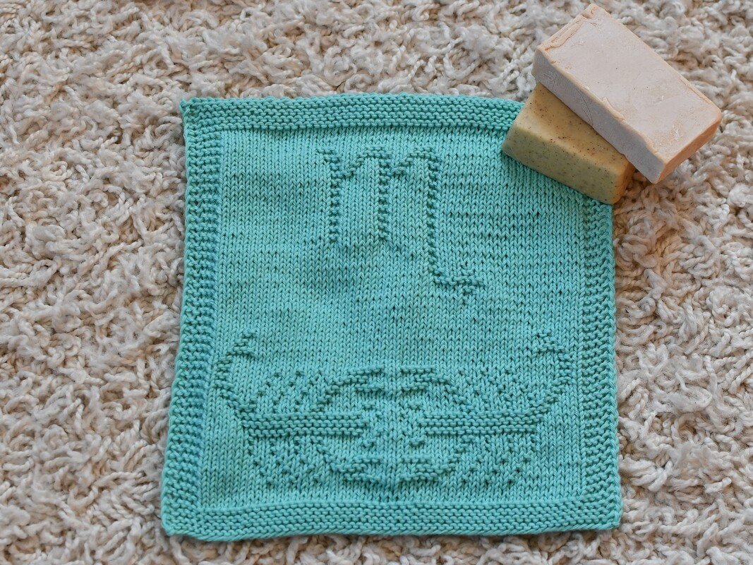 Türkises quadratisches Stricktuch mit Skorpion-Motiv und zwei Seifenstücken auf hellem Teppich