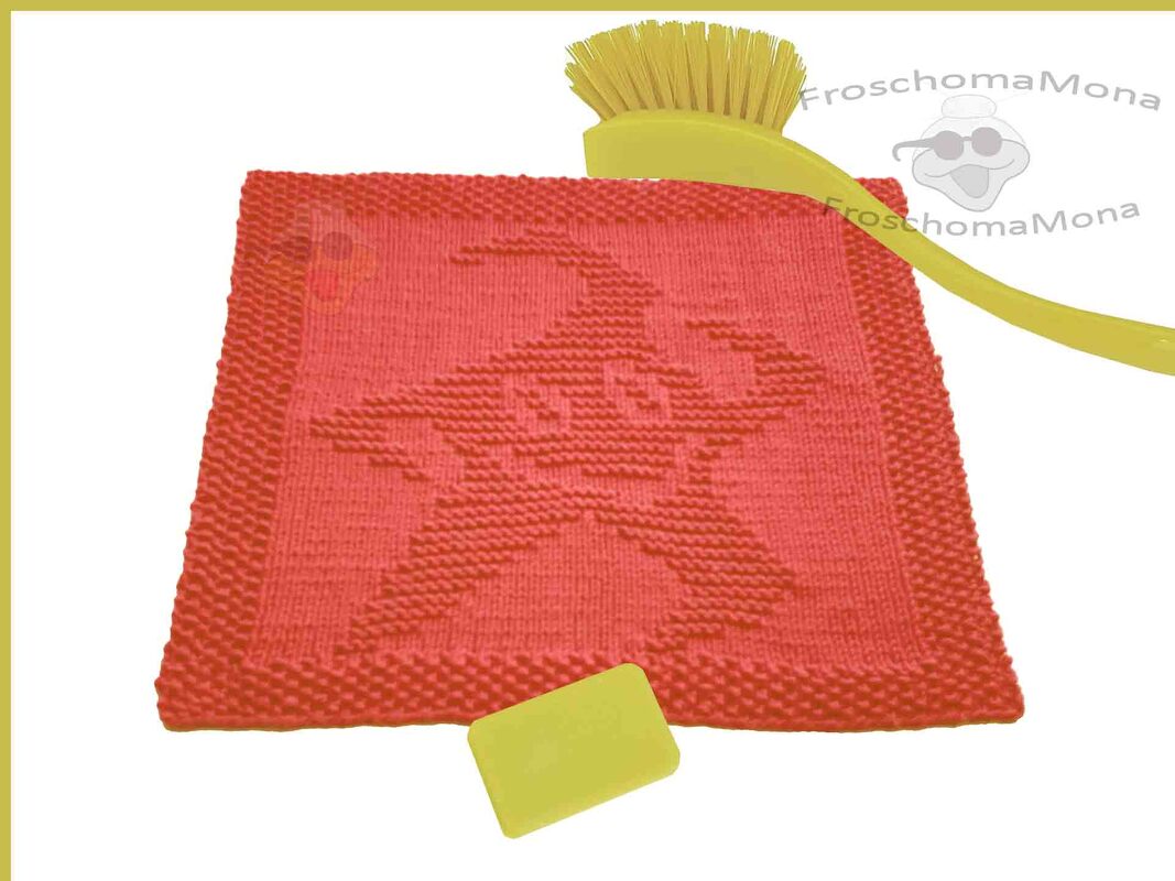 Rotes, quadratisches Stricktuch mit eingearbeitetem Froschmotiv, daneben eine gelbe Bürste und ein kleines gelbes Rechteck.