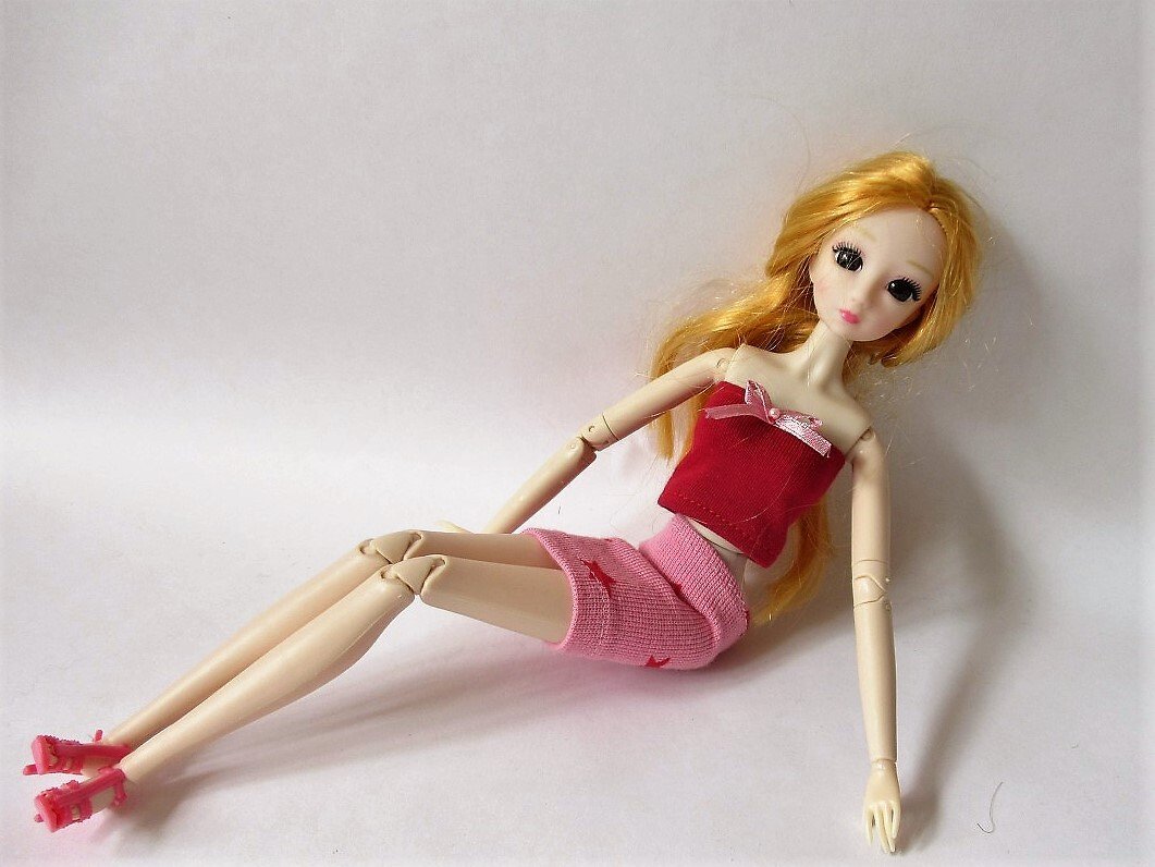 Puppe im roten Bandeau-Top und rosa gestricktem Minirock, liegend