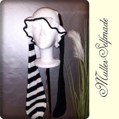 Gehäkelte schwarz-weiße Mütze mit Rüschenkrempe und langen Bändern auf Schaufensterpuppe