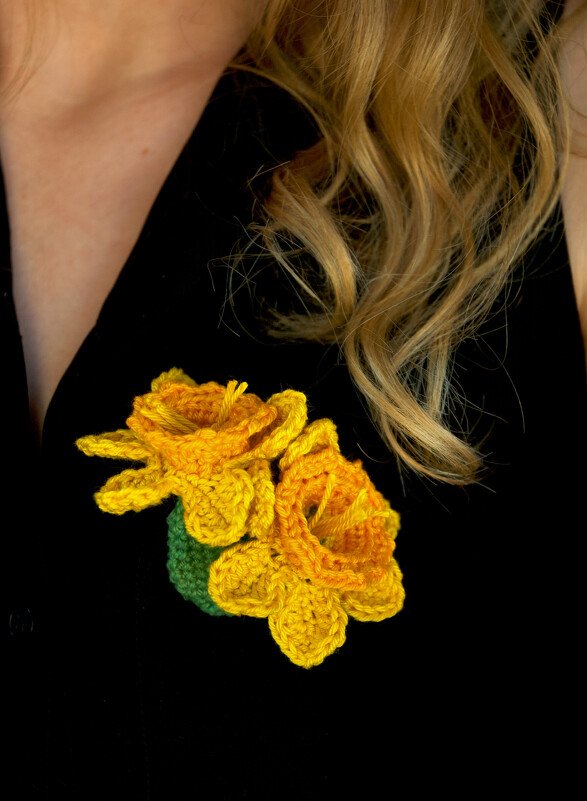 Yellow and orange crocheted daffodil brooch pinned to a black top.