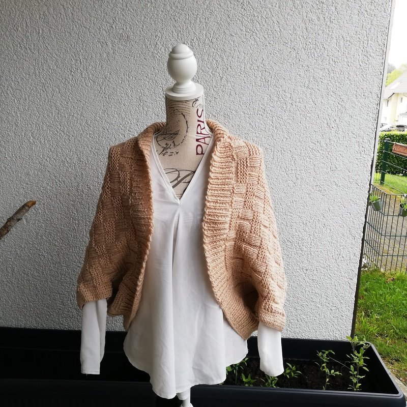 Kurze pfirsichfarbene Strickjacke mit Strukturmuster auf Schneiderpuppe über weißer Bluse