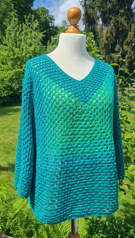 Gehäkelter Pullover in Türkis und Grün mit V-Ausschnitt auf einer Schaufensterpuppe vor grünem Garten