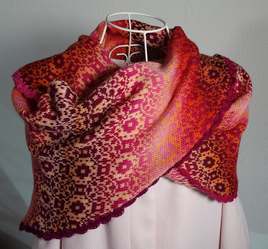 Gestricktes Dreieckstuch mit Jacquard-Muster in Pink-, Orange- und Gelbtönen auf Schneiderpuppe drapiert