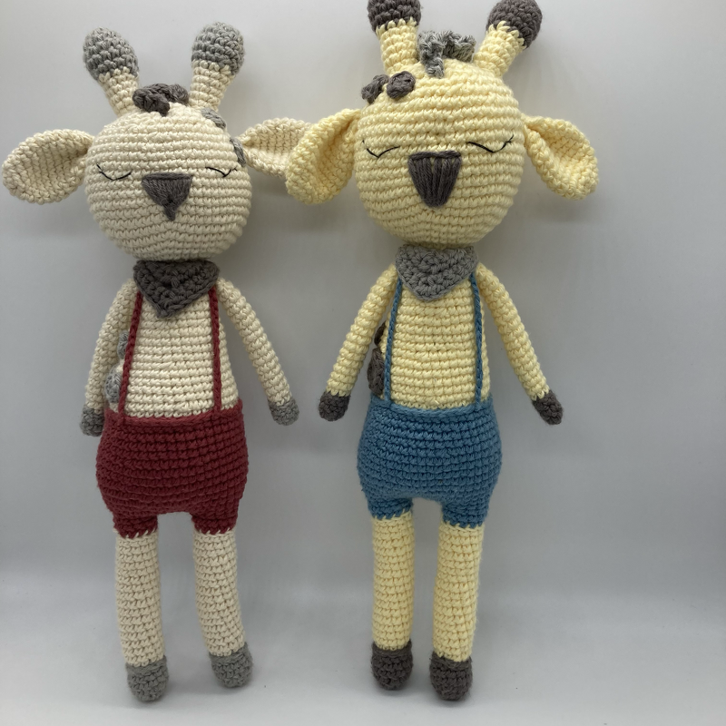 Zwei gehäkelte Giraffen-Amigurumi in Creme und Hellgelb mit geschlossenen Augen, Halstüchern und Hosenträgern