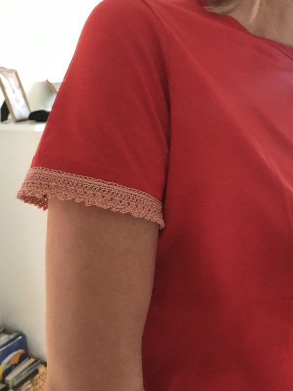 Nahaufnahme Ärmelabschluss mit pfirsichfarbener Häkelkante an rotem Shirt