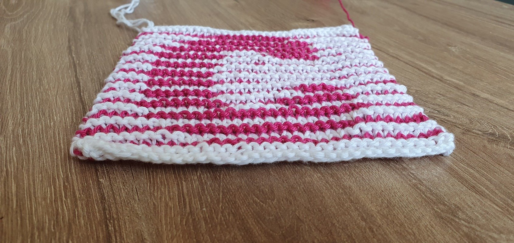 Gestricktes Quadrat mit rosa-weißem Herzmuster auf Holz