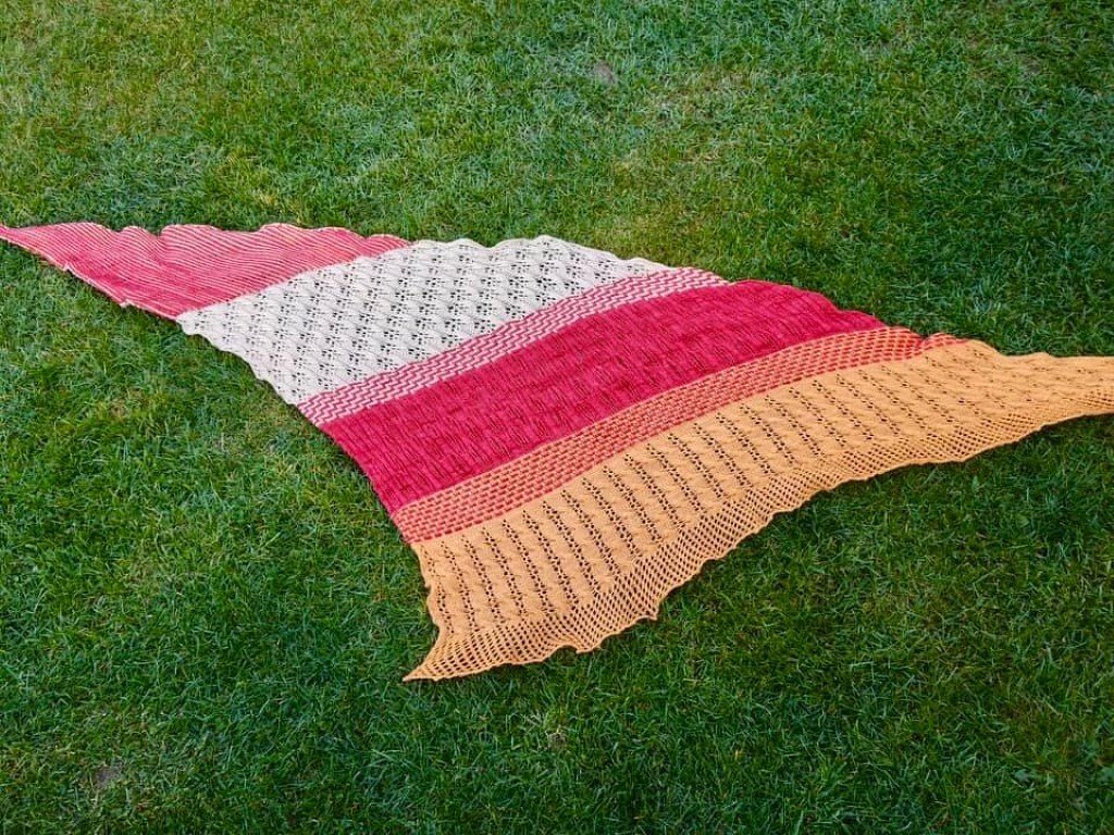 Buntes gestricktes Dreieckstuch mit Lochmuster und Streifen auf Rasen ausgebreitet