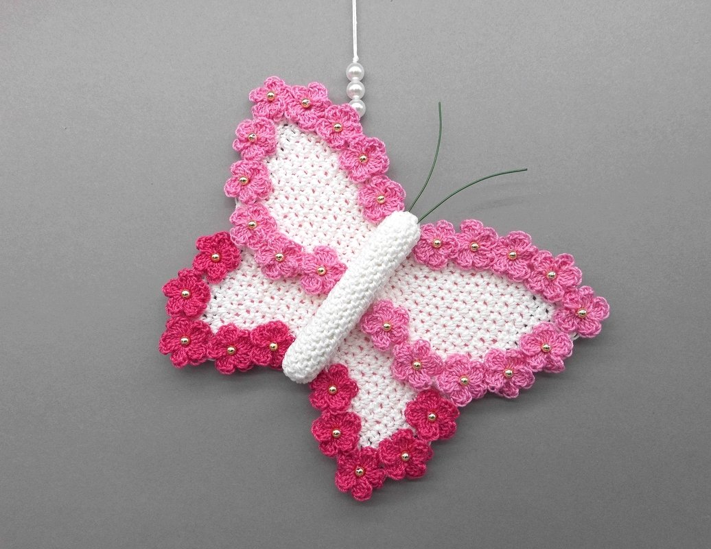 White crochet butterfly ornament with pink floral scalloped edges and gold beads on gray background