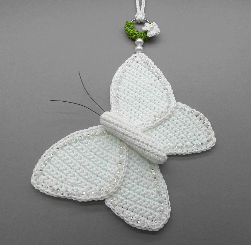 White crocheted butterfly ornament with beaded wing edges, wire antennae, and a decorative hanger with a green wreath and pearls.
