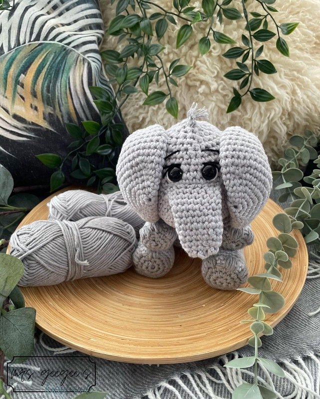 Grau gehäkelter Amigurumi‑Elefant mit Garnknäueln auf Holzschale