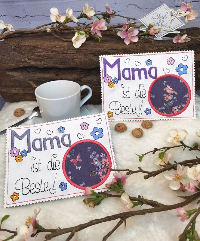 Zwei bestickte Tassenteppiche mit Schriftzug 'Mama ist die Beste', Blumenstickereien und runden Tier-Applikationen (Vogel und Schmetterling) neben einer weißen Tasse