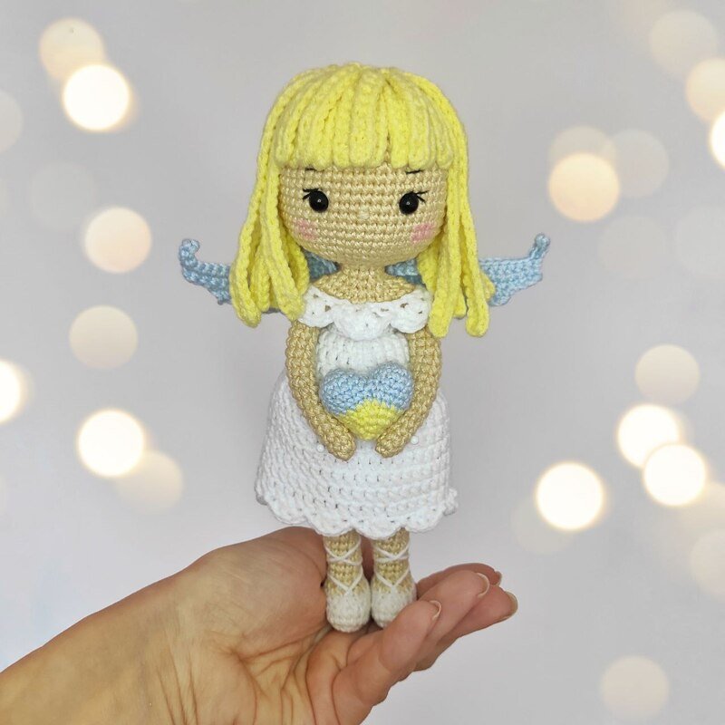 Palm-sized amigurumi angel in hand showing stitch detail, scalloped white dress, blue wings and yellow hair