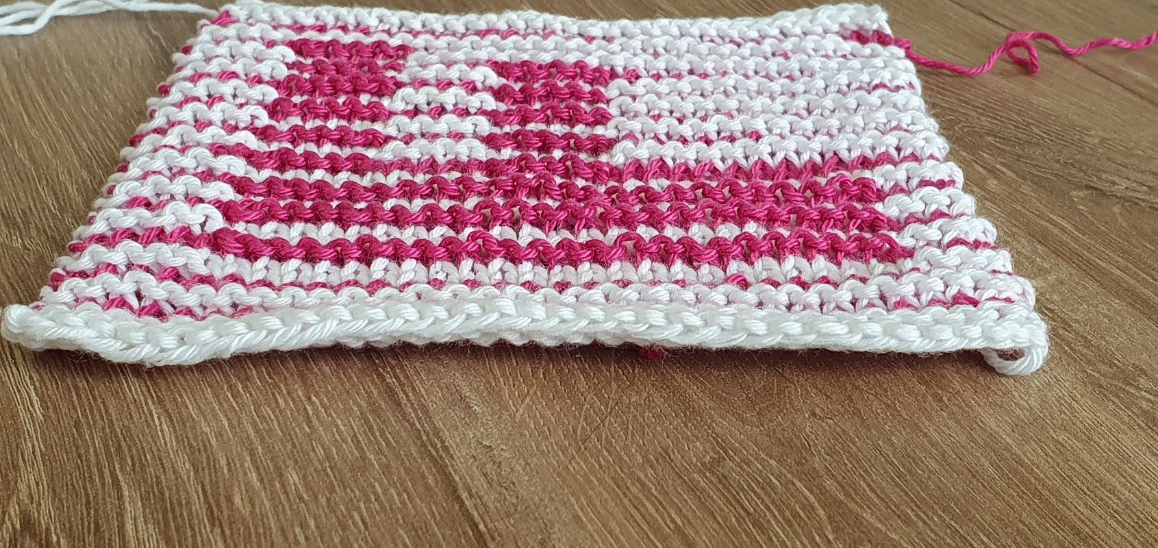 Nahaufnahme einer rechteckigen gestrickten Maschenprobe in Weiß und Pink, kraus rechts