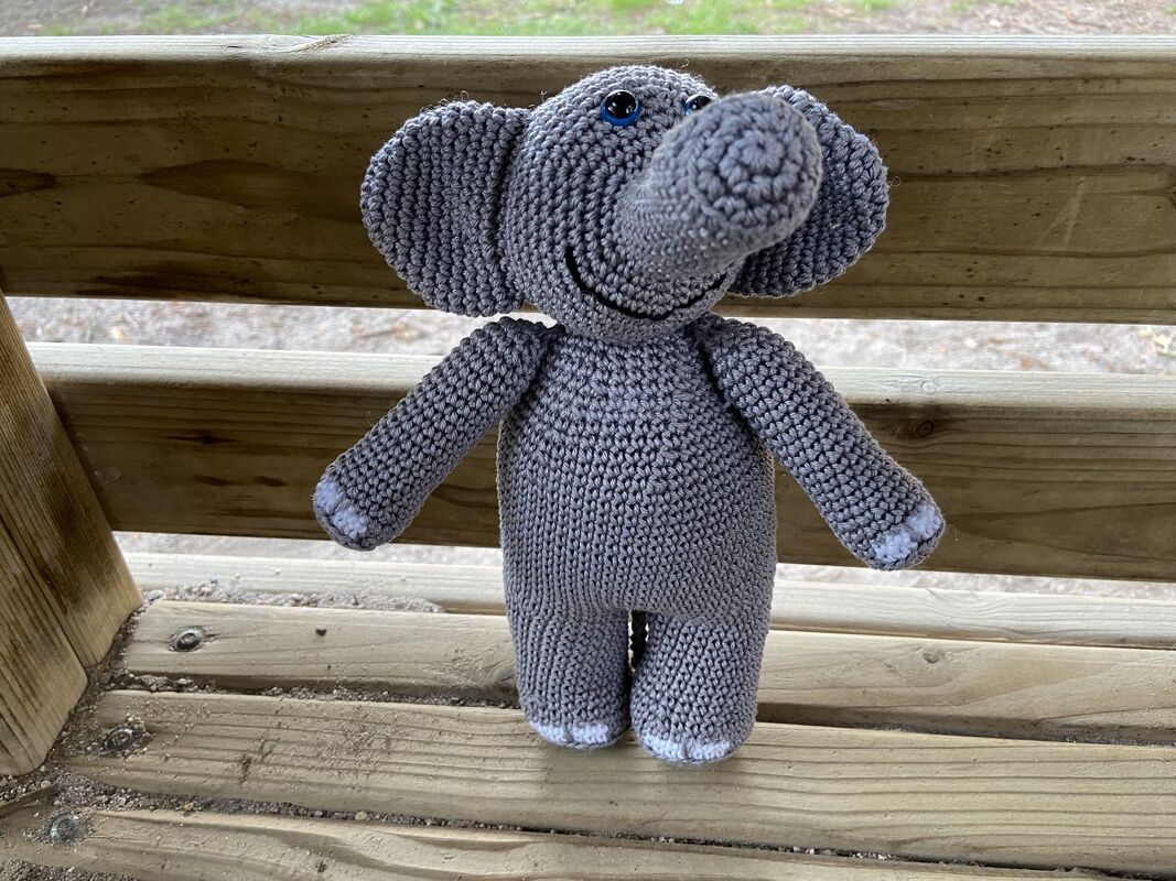 Grau gehäkelter Amigurumi‑Elefant mit großen Ohren auf Holzbank